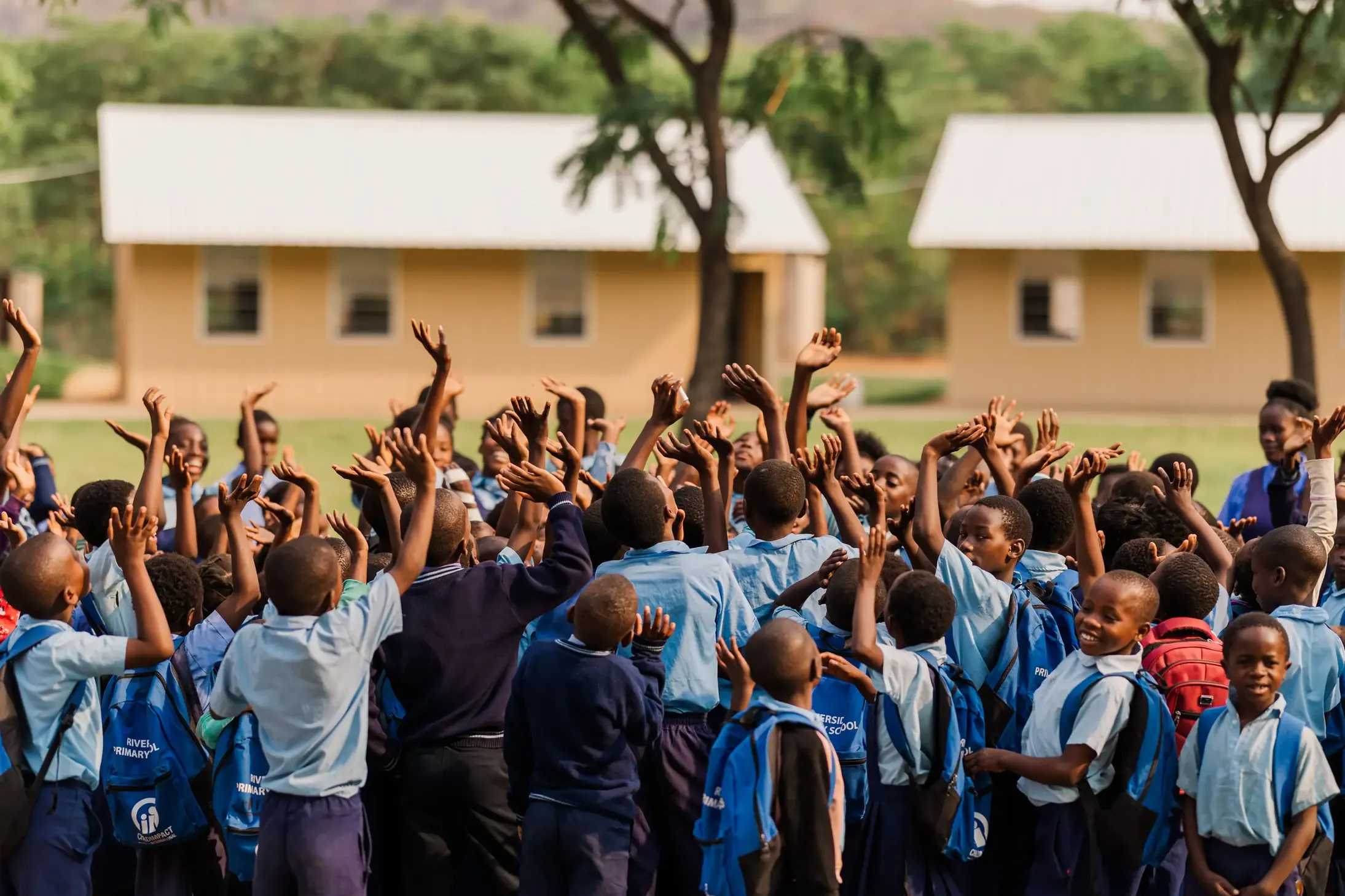 A group of student gathered in a circle celebrating, lifting their arms to the sky.